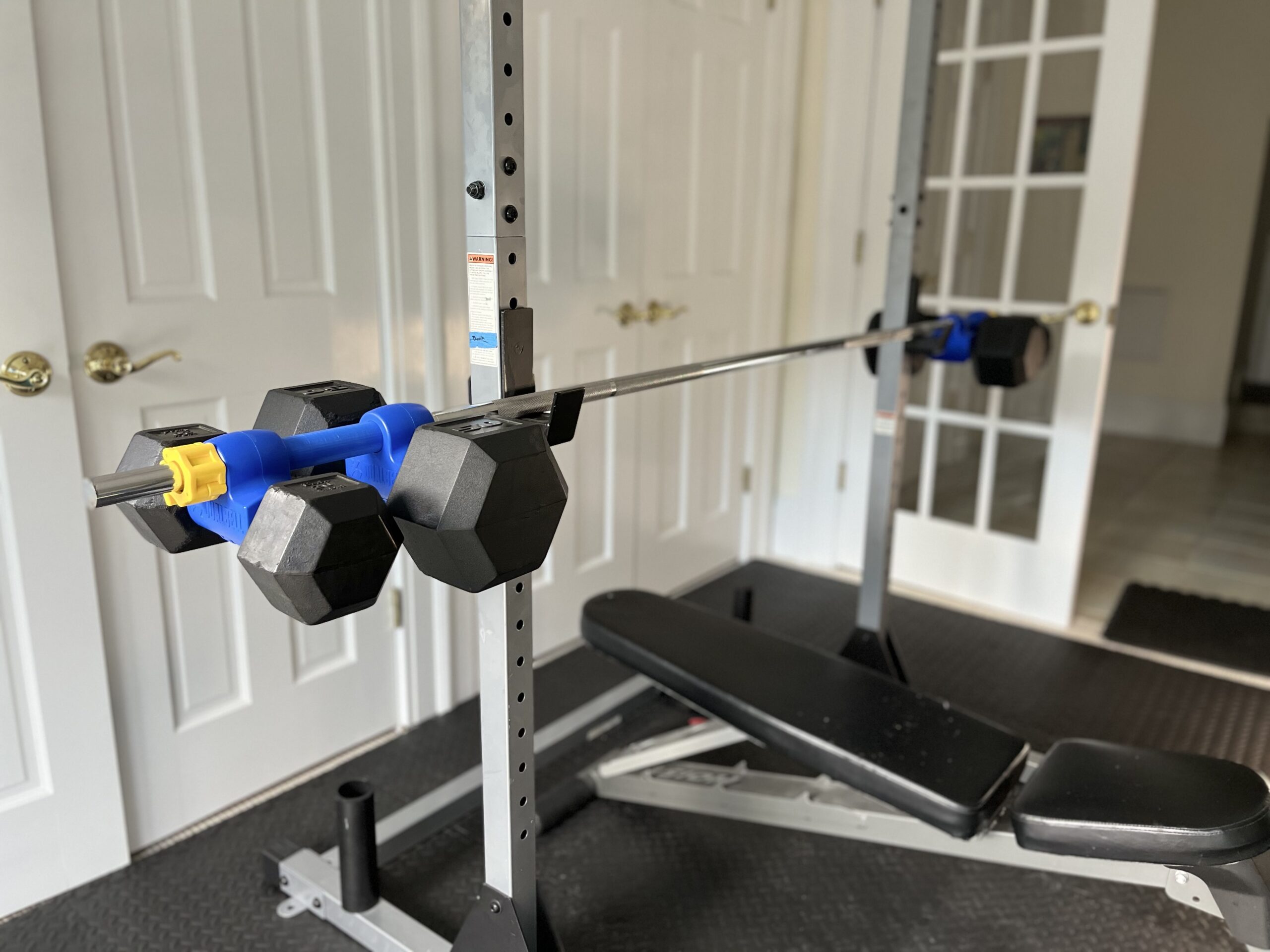 Dualbell shown in home gym holding four dumbbells on a barbell ready for bench press.